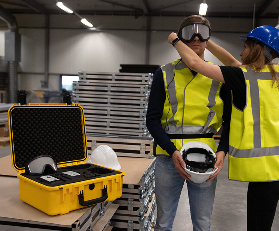 Twee personen in een industriële omgeving testen veiligheidsuitrusting, waaronder brillen en helmen, met een stevige beschermkoffer op de voorgrond.