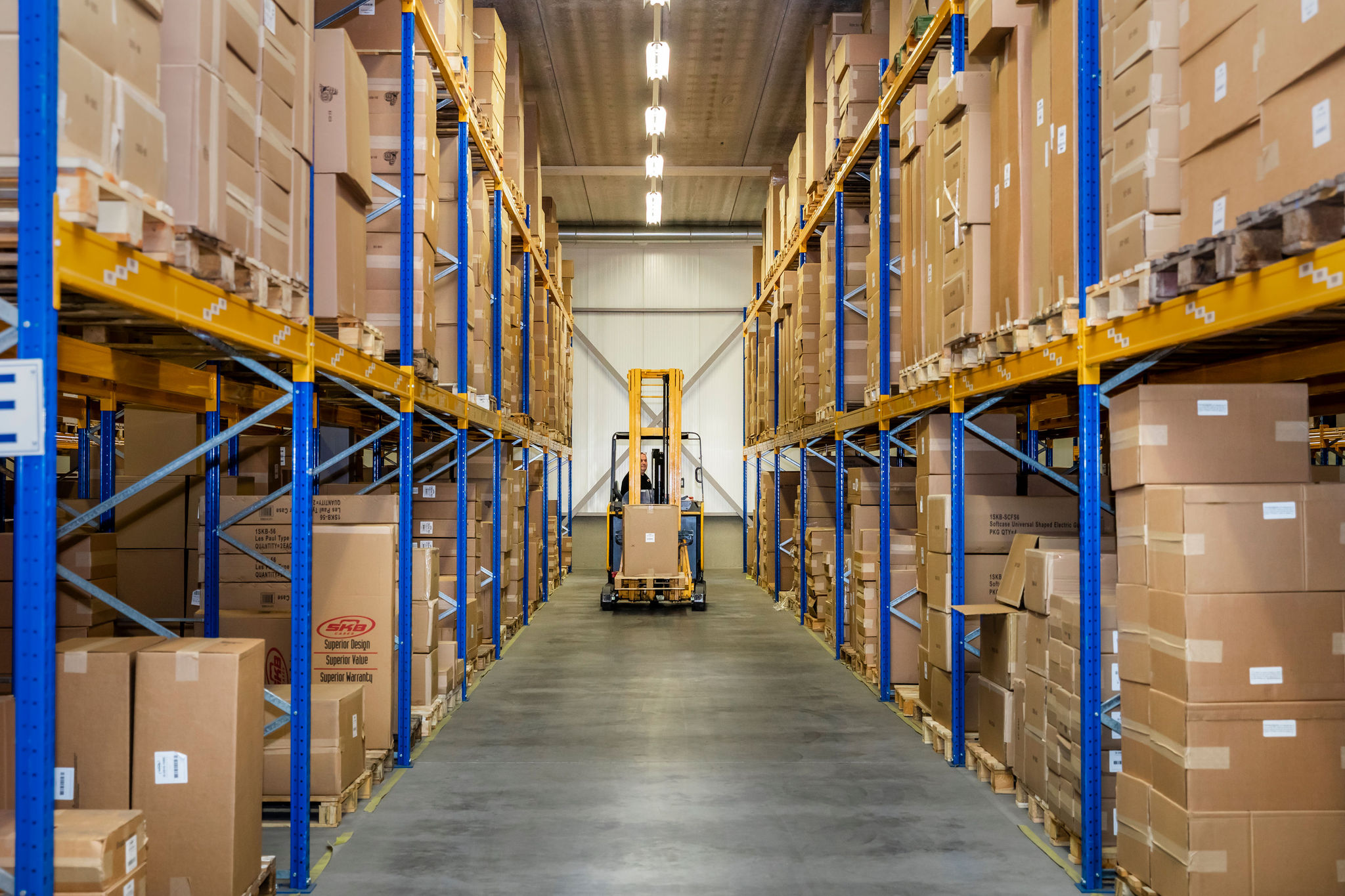 Magazijn van Faes met stellingen vol dozen en heftruck in gangpad