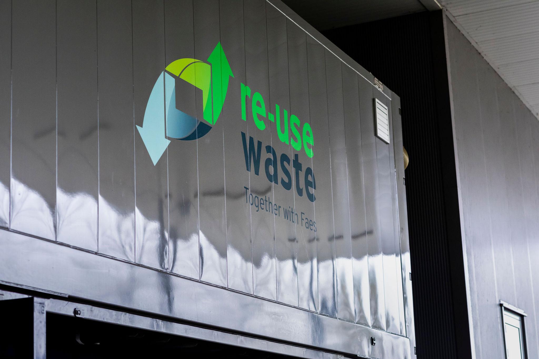 Close-up van een container met het logo "Re-use Waste" en de tekst "Together with Faes", die duurzame samenwerking benadrukt.