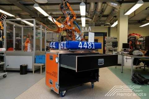 Een op maat gemaakte oranje flightcase, met een robot veilig opgeborgen in de koffer en een uitgeschoven lade voor extra opslag. Ideaal voor het veilig vervoeren en opstellen van technische apparatuur tijdens wedstrijden.