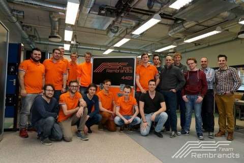 Groepsfoto van Team Rembrandts & Faes voor hun speciaal ontworpen flightcase, met teamleden in oranje shirts en de flightcase prominent op de achtergrond. De flightcase draagt het logo van Team Rembrandts en is bedoeld voor veilig transport van technische uitrusting tijdens wedstrijden.