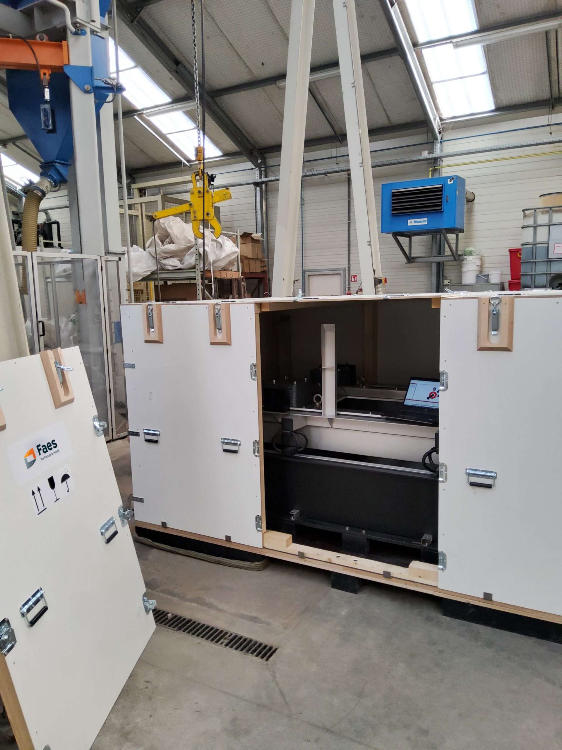 Geopende houten maatwerk kist van Faes, ontworpen voor het veilig transporteren van industriële apparatuur. De kist toont een nauwkeurig ingepakte technische installatie, met stevige metalen sluitingen en beschermingsmateriaal om schokken en trillingen tijdens vervoer op te vangen. Perfect voor het transporteren van delicate technische componenten.