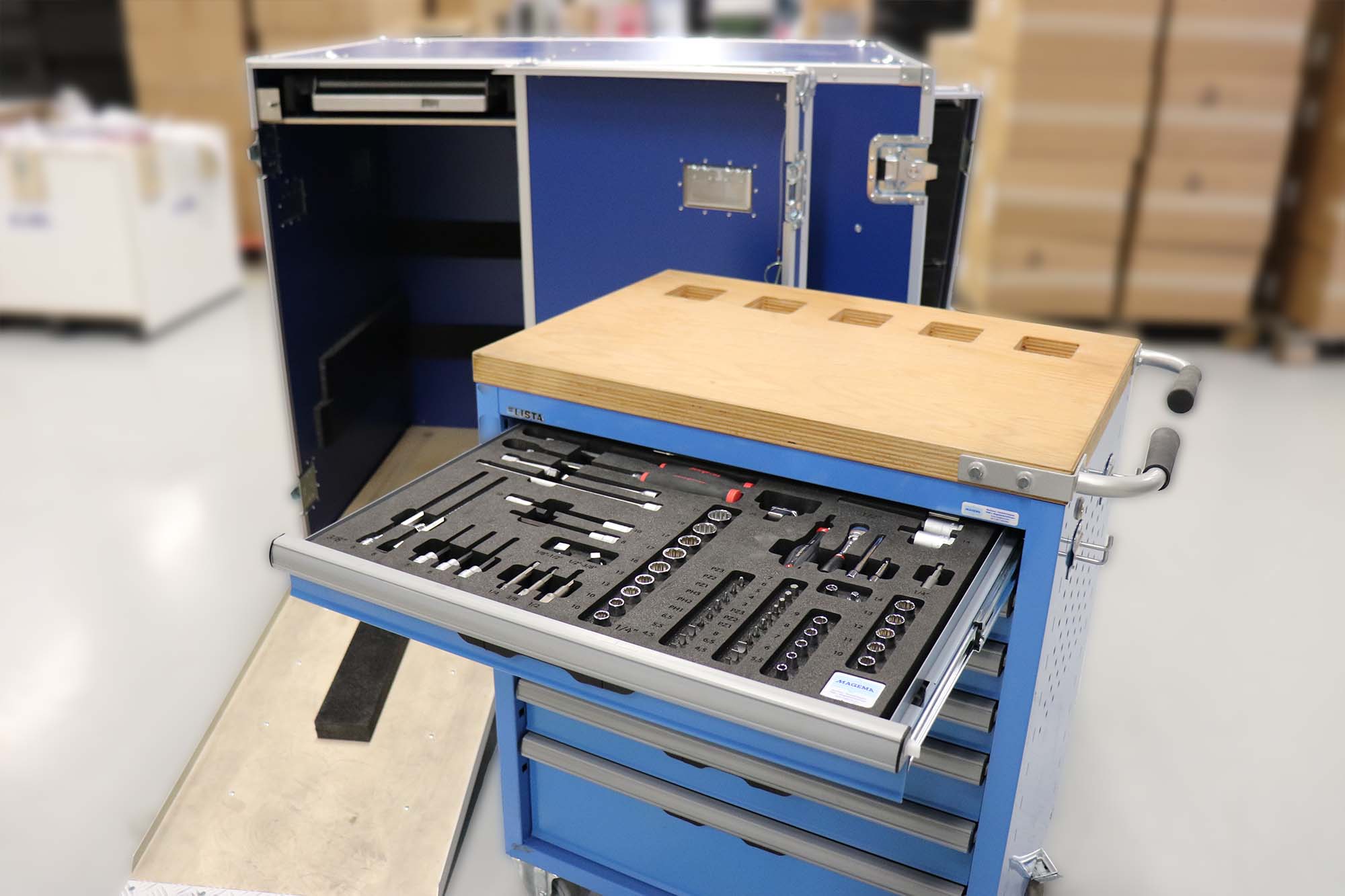Een toolkit netjes georganiseerd in een lade van een mobiele werkplaats, opgeslagen in een stevige blauwe flightcase. De toolkit bevat verschillende gereedschappen en instrumenten, speciaal ontworpen voor gebruik in de medische sector. De flightcase is open, met een duidelijk overzicht van de inhoud en een houten werkblad aan de bovenkant van de gereedschapswagen.