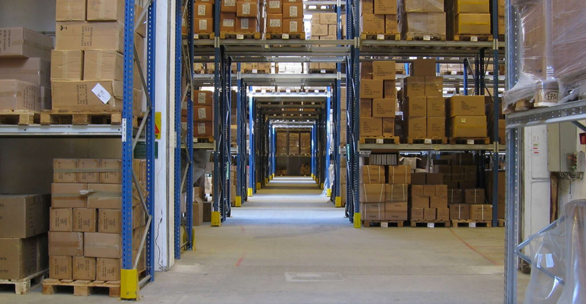 Grote opslagruimte met gestapelde dozen op pallets in hoge stellingen, een voorbeeld van efficiënt magazijnbeheer dat integraal is binnen retourlogistieke processen.