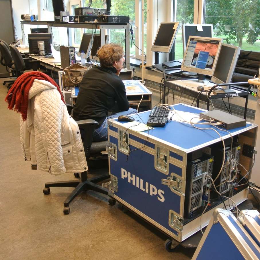 Flightcase met IT-apparatuur van Philips in gebruik, opgesteld naast werkstations in een kantooromgeving voor ondersteuning van technische projecten.